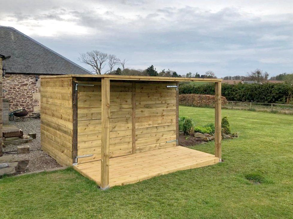A wooden shed is sitting in the middle of a lush green field.