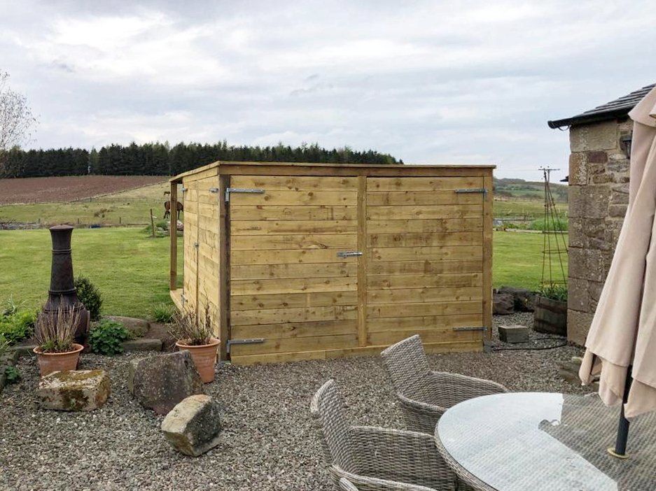 A wooden shed is sitting in the middle of a gravel yard next to a table and chairs.