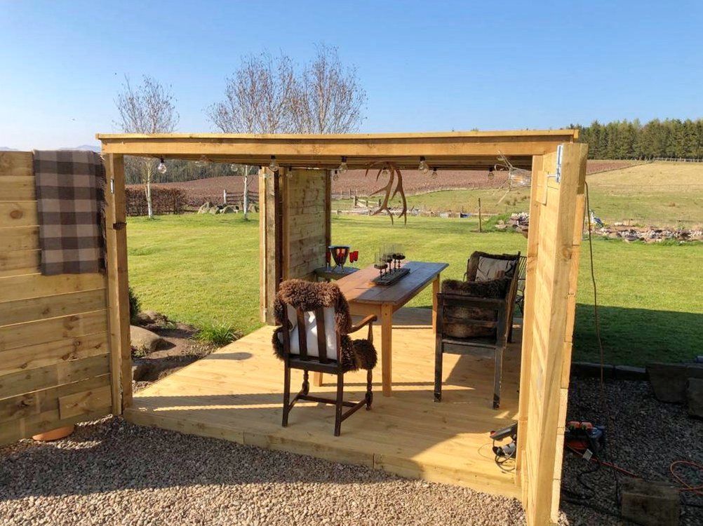 A wooden shed with a table and chairs in the middle of a field.