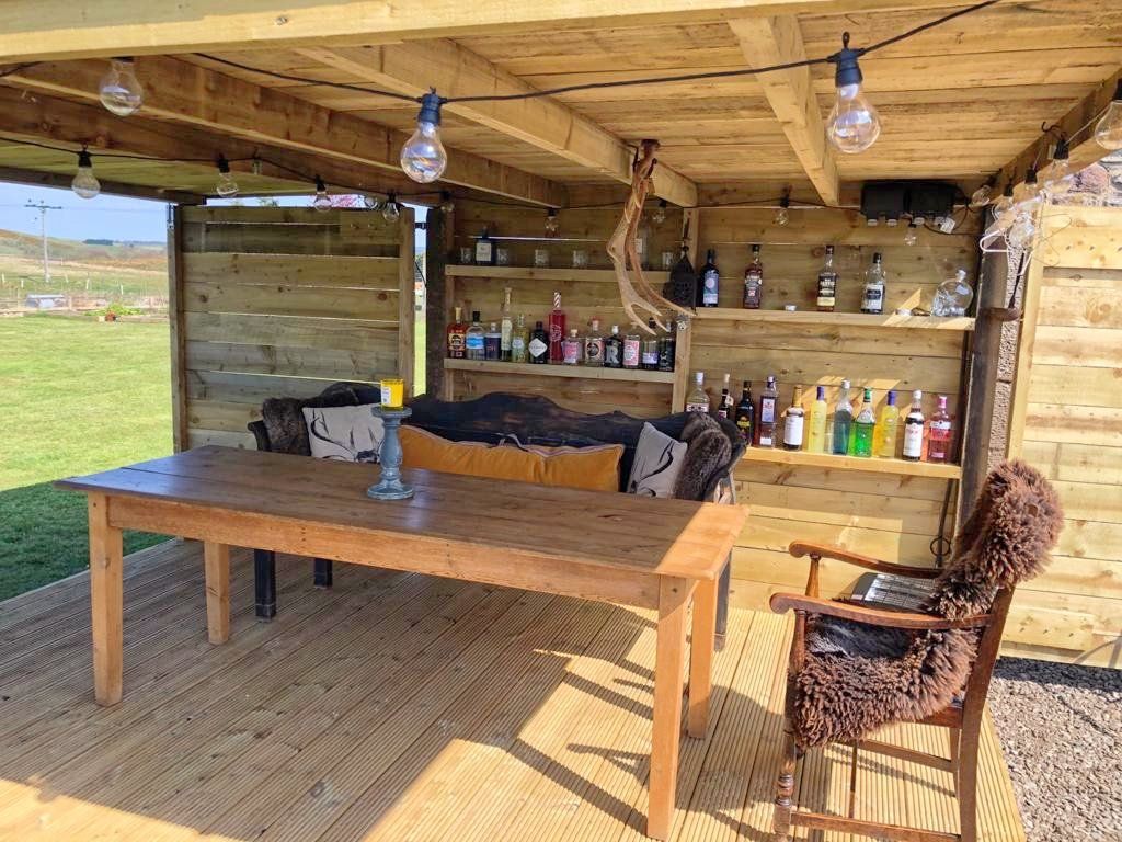 A wooden shed with a table , chairs and shelves filled with bottles of alcohol.
