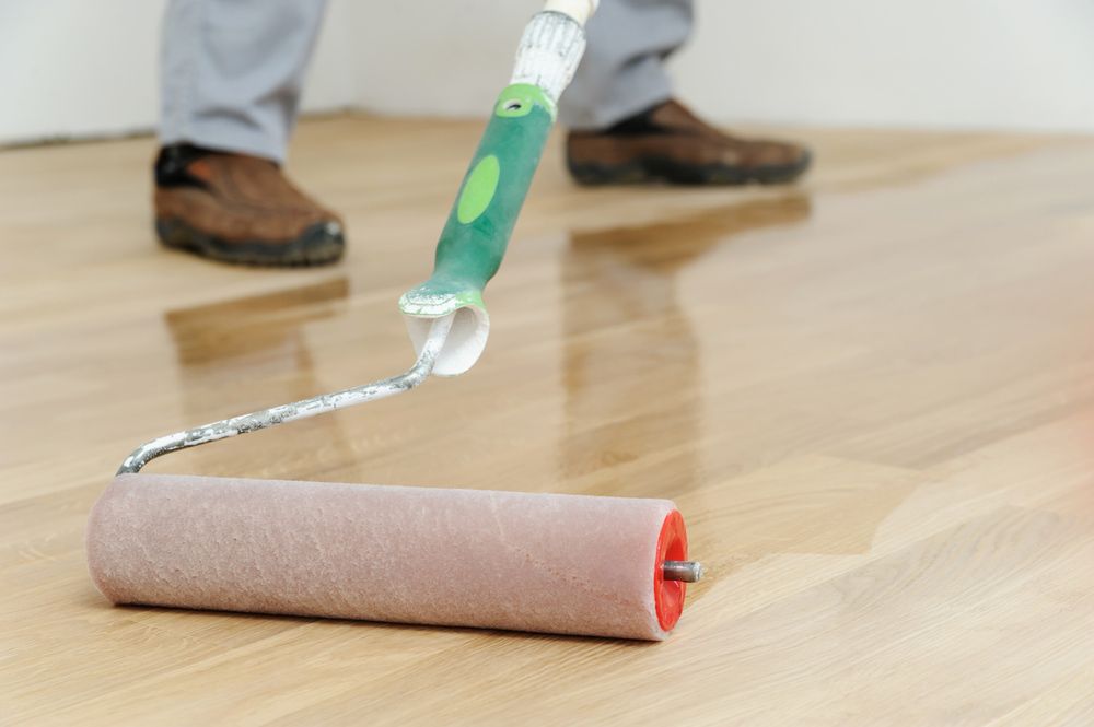 A Person Is Painting A Wooden Floor With A Roller — Byron Floor Sanding In Lismore, NSW