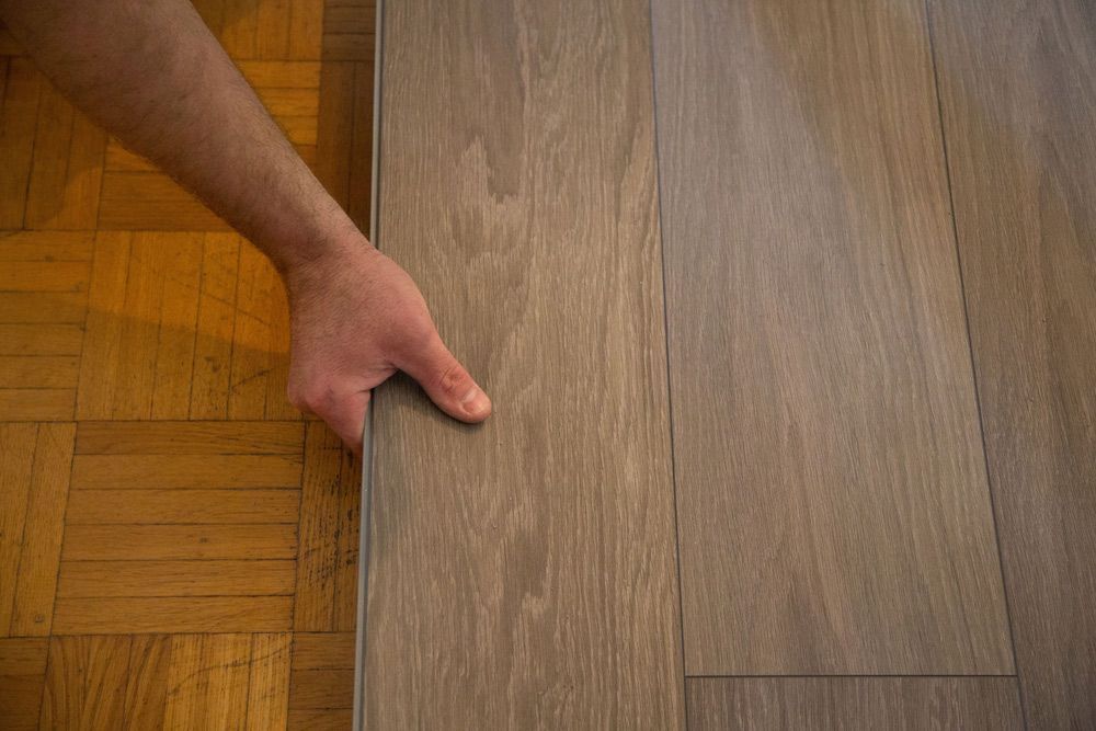 A Person Is Pointing At A Piece Of Wood On A Wooden Floor — Byron Floor Sanding In Byron Bay, NSW