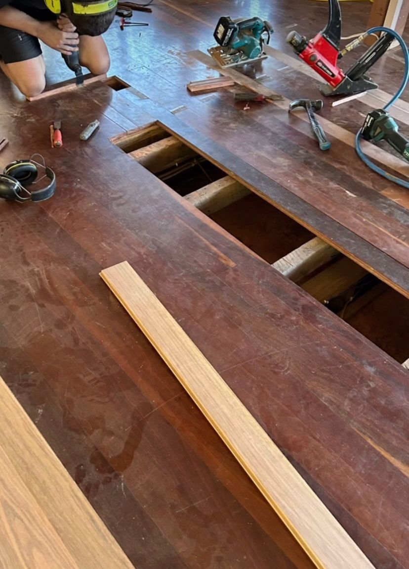 A Man is Working On Repairing Wooden Floor Boards with Power Tool on the Floor — Byron Floor Sanding In Byron Bay, NSW