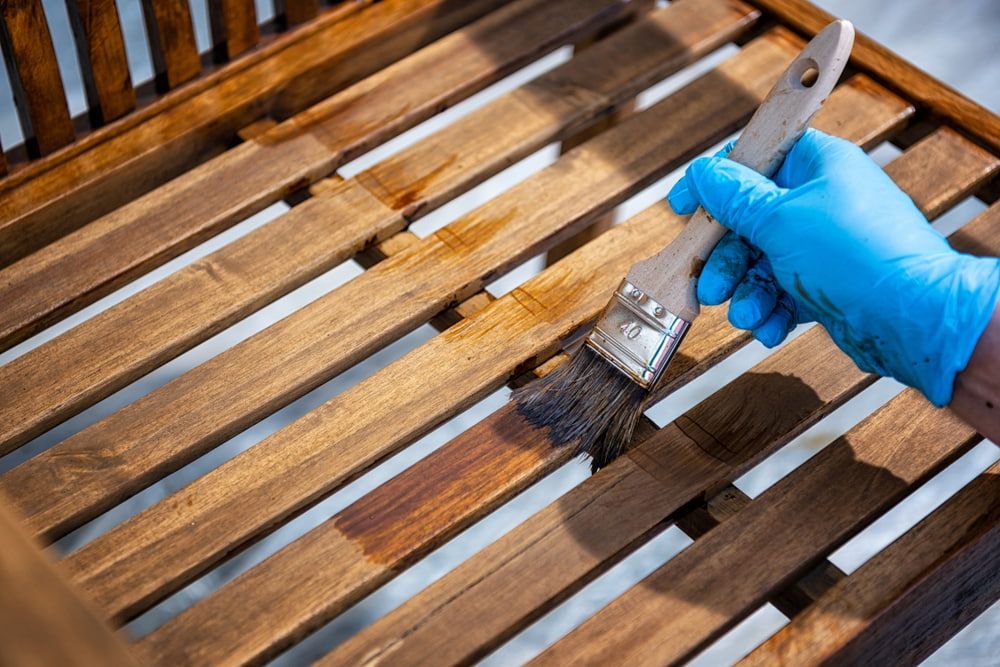 Person in Blue Glove Staining Wooden Bench with A Brush — Byron Floor Sanding In Tintenbar, NSW