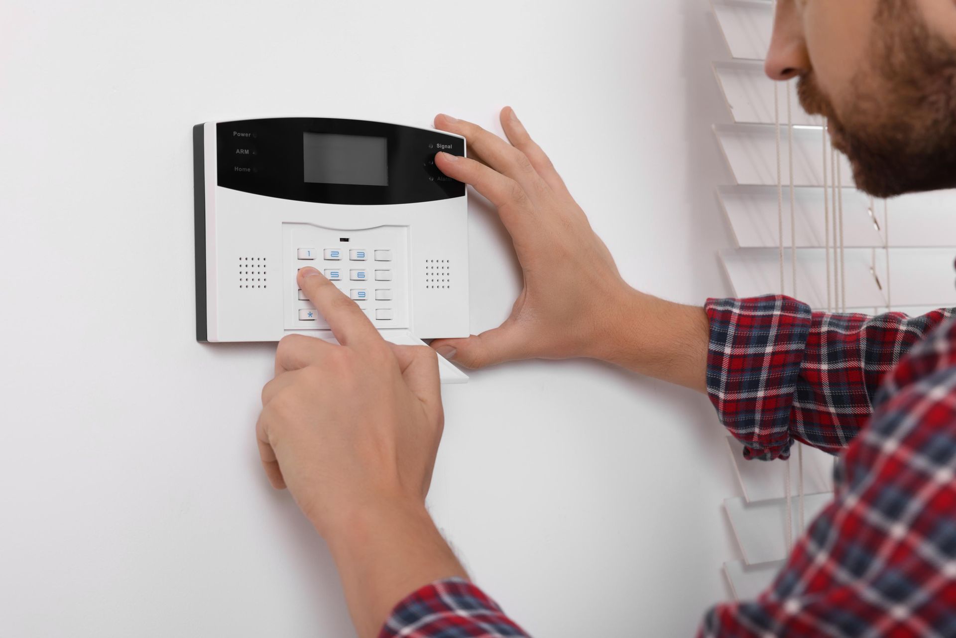 Person pressing buttons on a security system keypad mounted on a white wall.