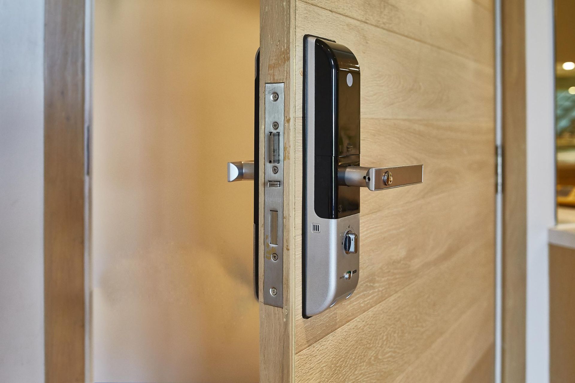 Door with a smart lock, open slightly, showing lock's handle and metal latch against a light wooden door.