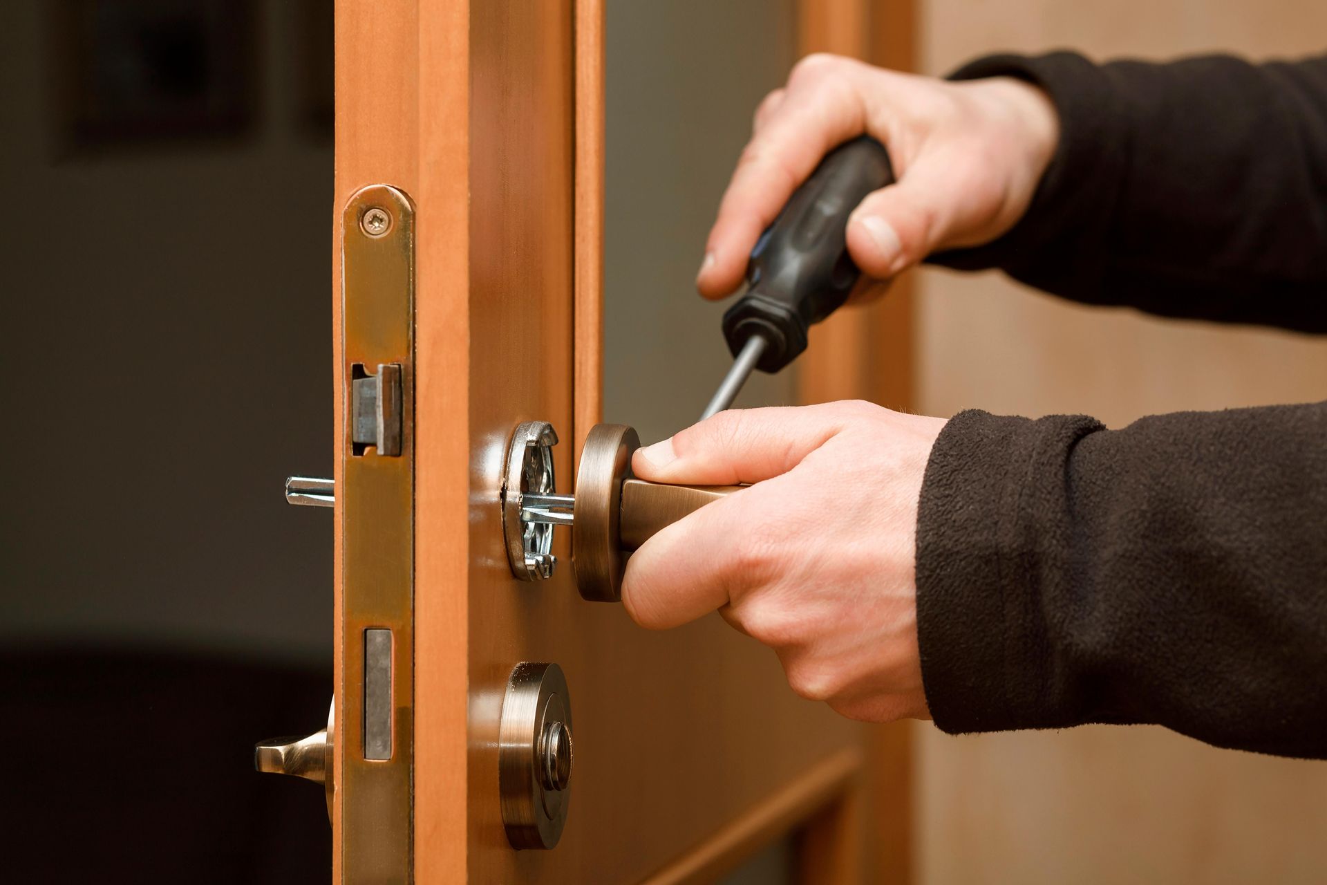 Person using a screwdriver to install or repair a door lock on a wooden door.