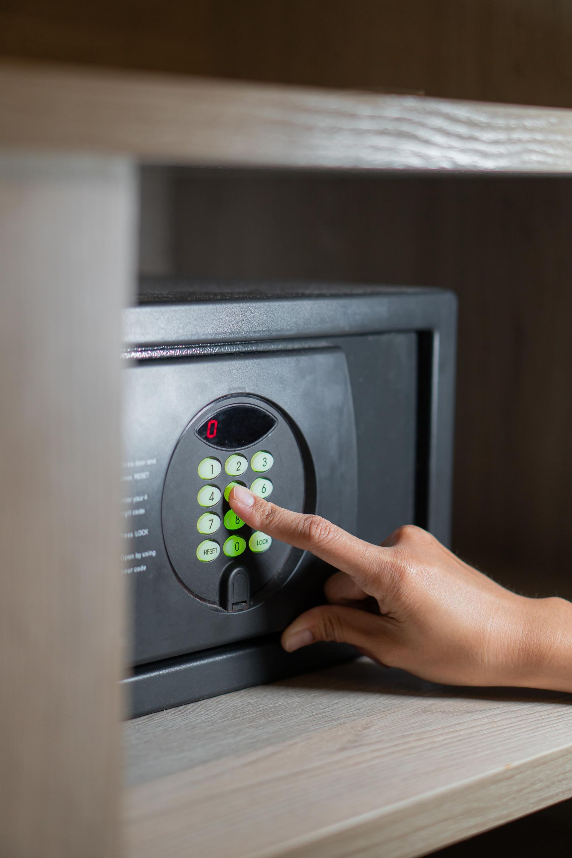 Hand entering a code on a digital keypad of a black safe inside a wooden shelf.