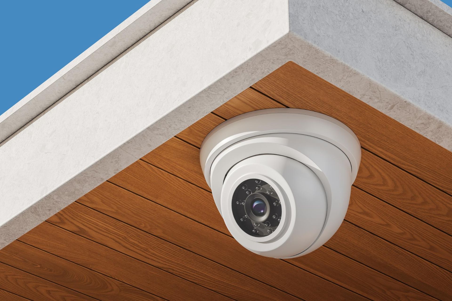 White security camera mounted on a brown wooden ceiling, under a white overhang.