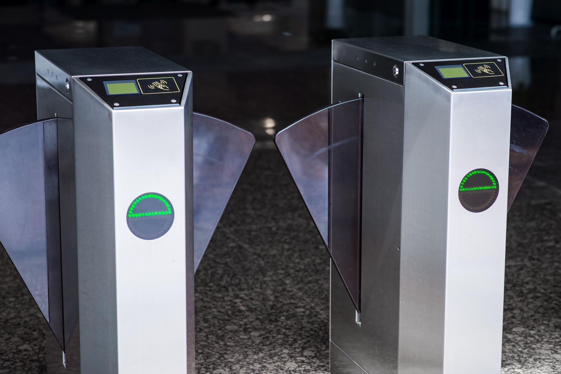 Two silver turnstiles with green circular indicators, likely for access control in a building.