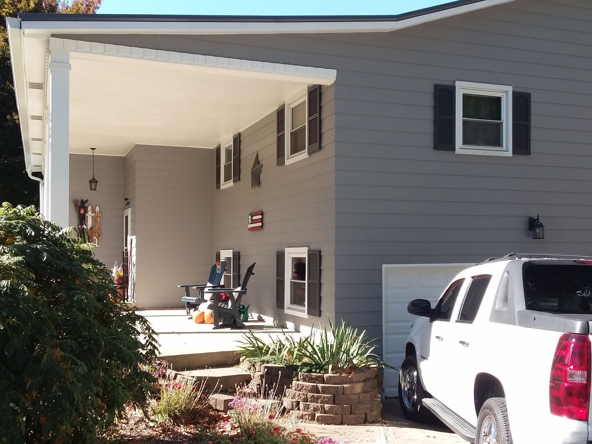 A grey house exterior featuring a covered porch, a white pickup truck parked in the driveway, and a stone garden bed.