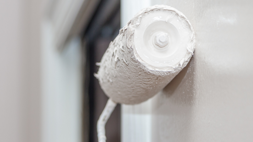 Paint roller applying white paint to a wall.