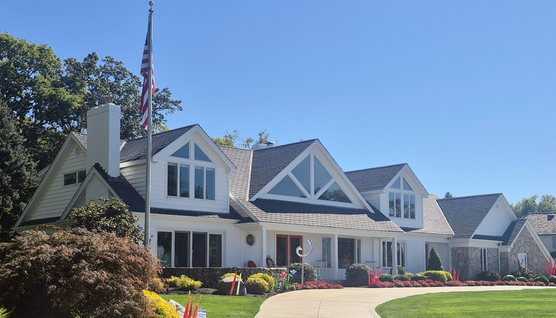 A large, white multi-story house with a peaked roof, dormer windows, and an American flag on a front lawn.