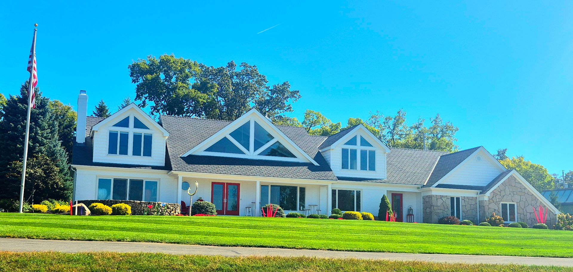 A long, white, multi-gabled house with grey roofing, large windows, and a tall American flag flying on the left.
