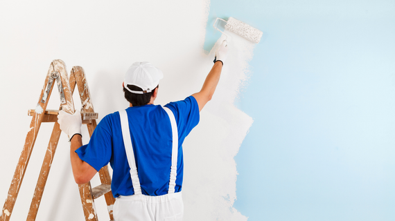 Painter on a ladder, rolling white paint over a wall, transitioning from light blue.