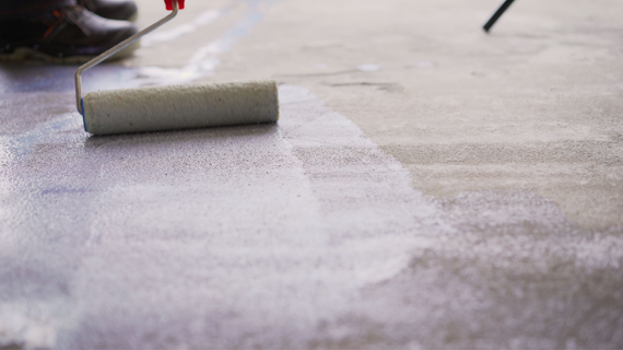 Person rolling white paint on a concrete floor.