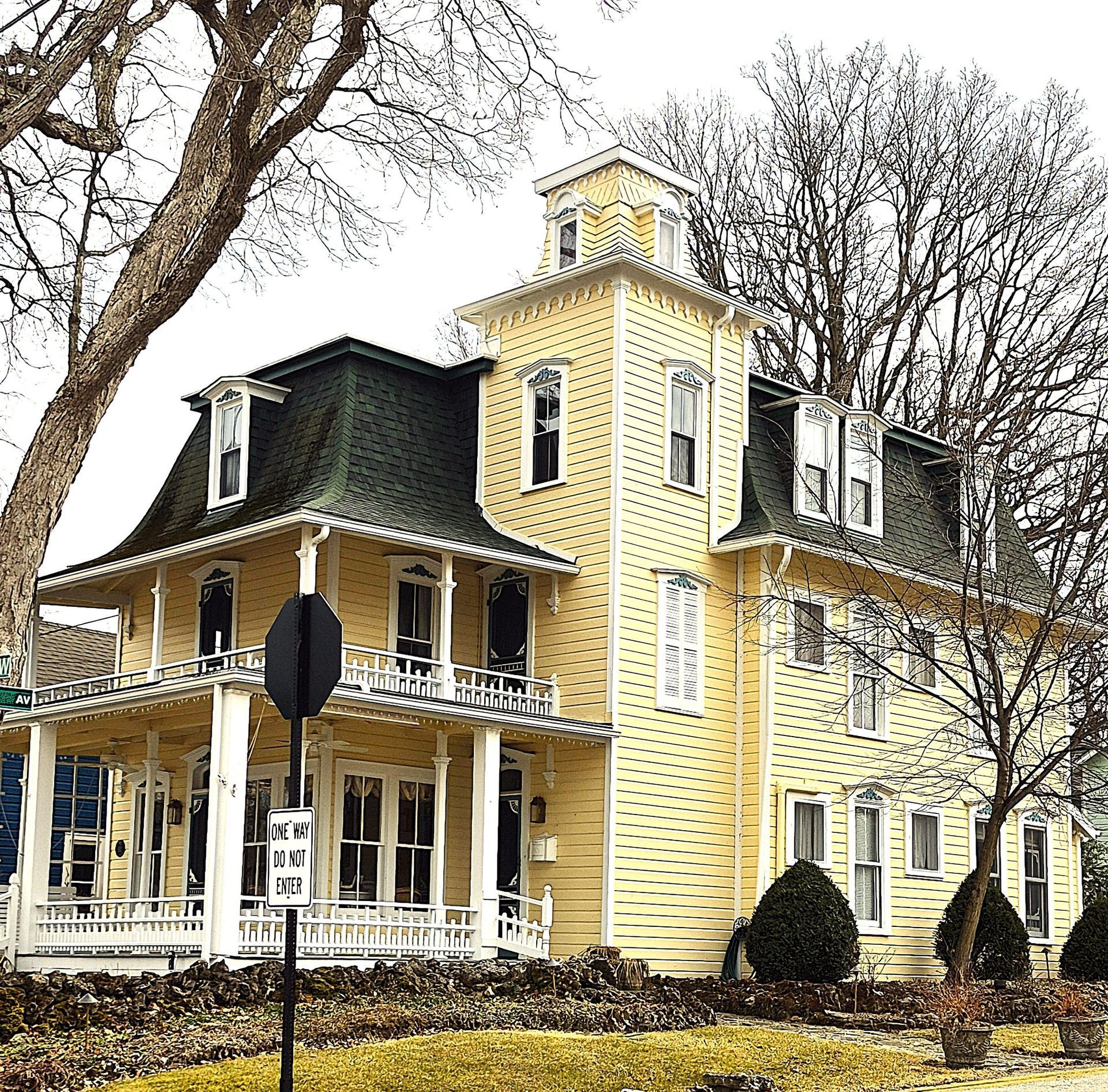 A yellow Victorian-style house with a dark mansard roof, a central tower, and a wrap-around porch.