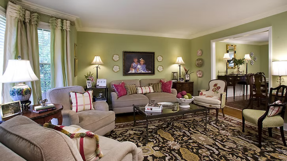 Living room with light green walls, couches, chairs, area rug, lamps, and decorative plates.