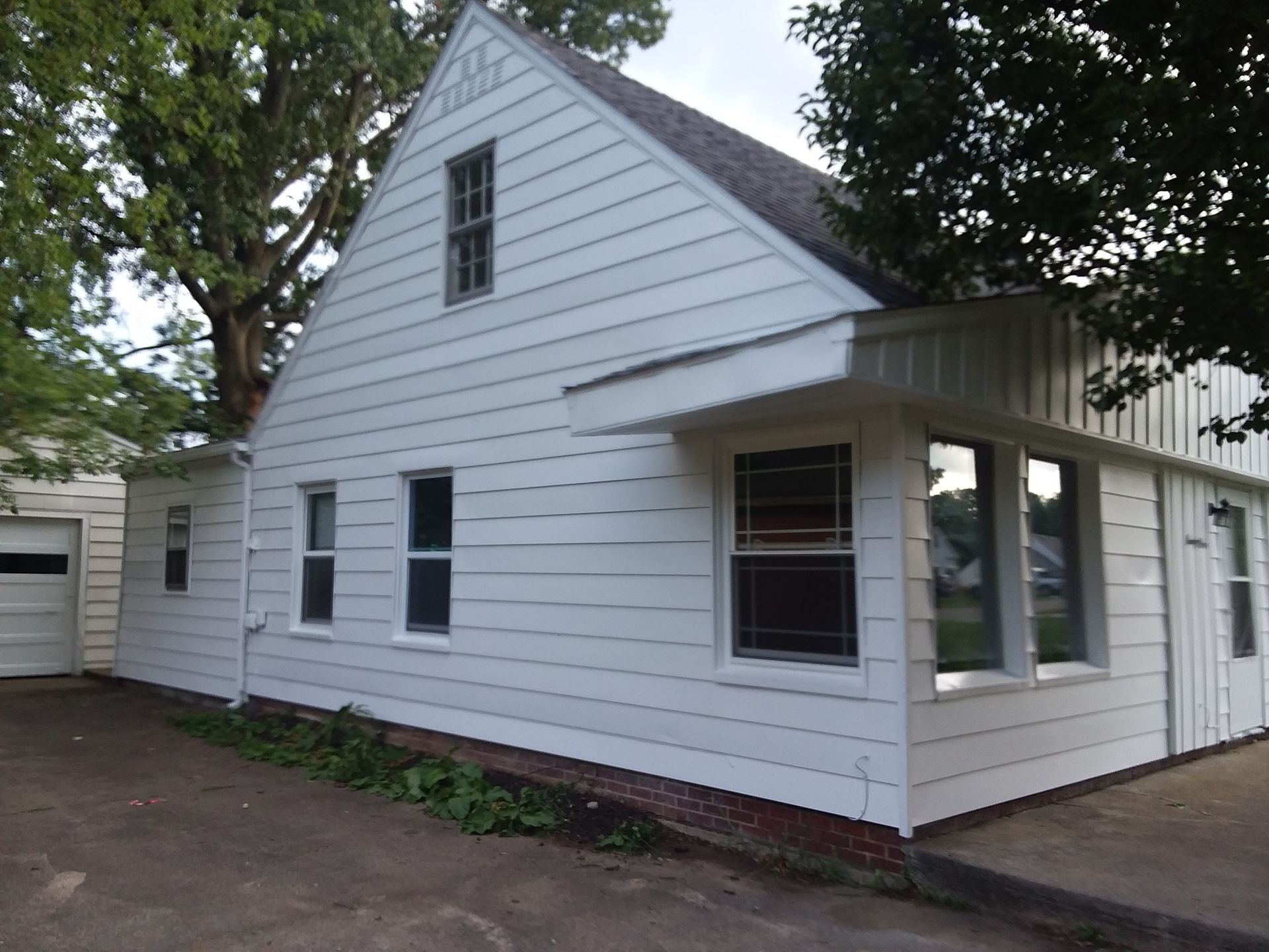 A white, single-story house with a gabled roof, horizontal siding, and a detached garage on a paved lot.
