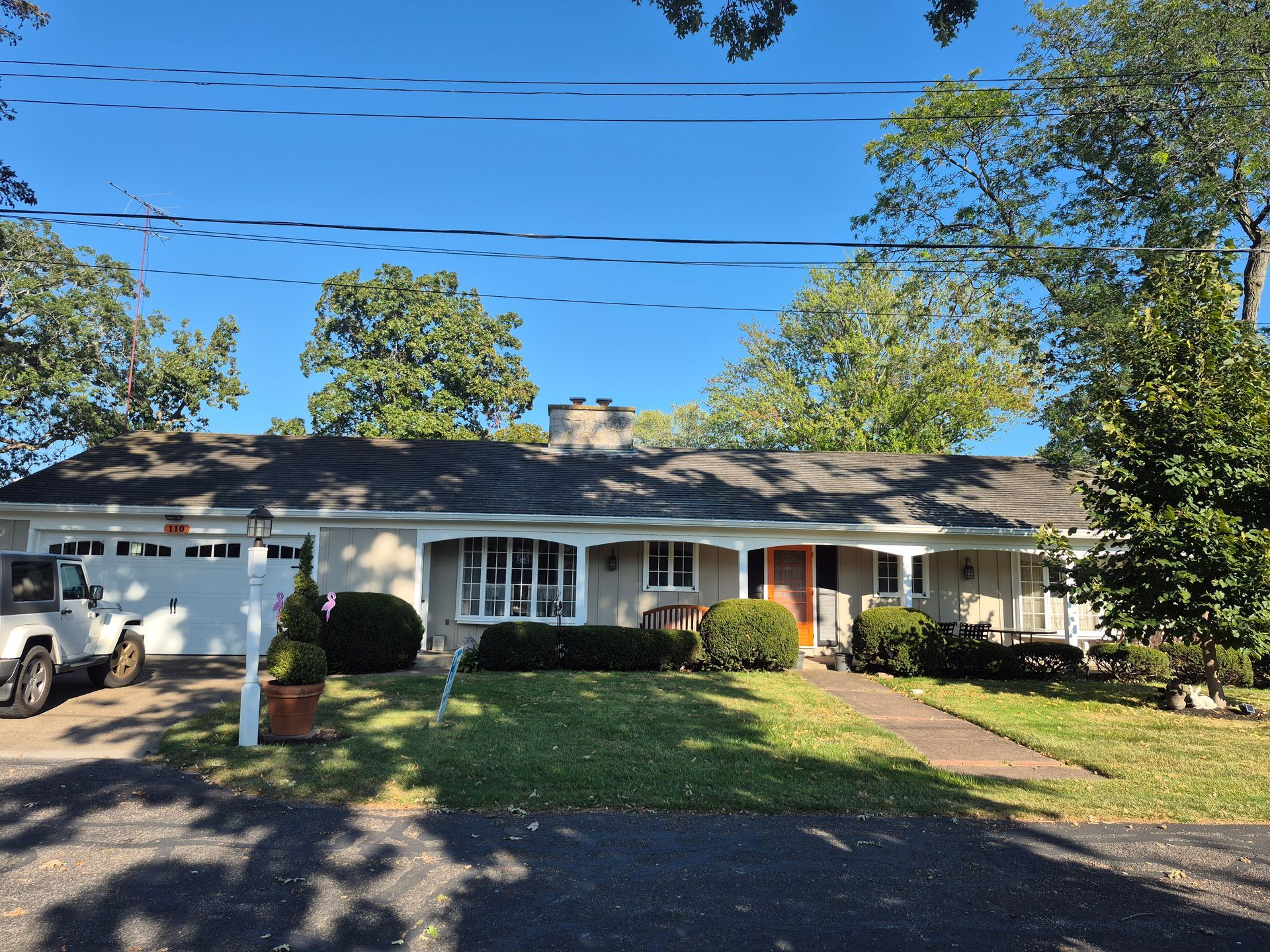 A single-story ranch house with a white garage, a wide covered porch, and green lawn under a clear blue sky.
