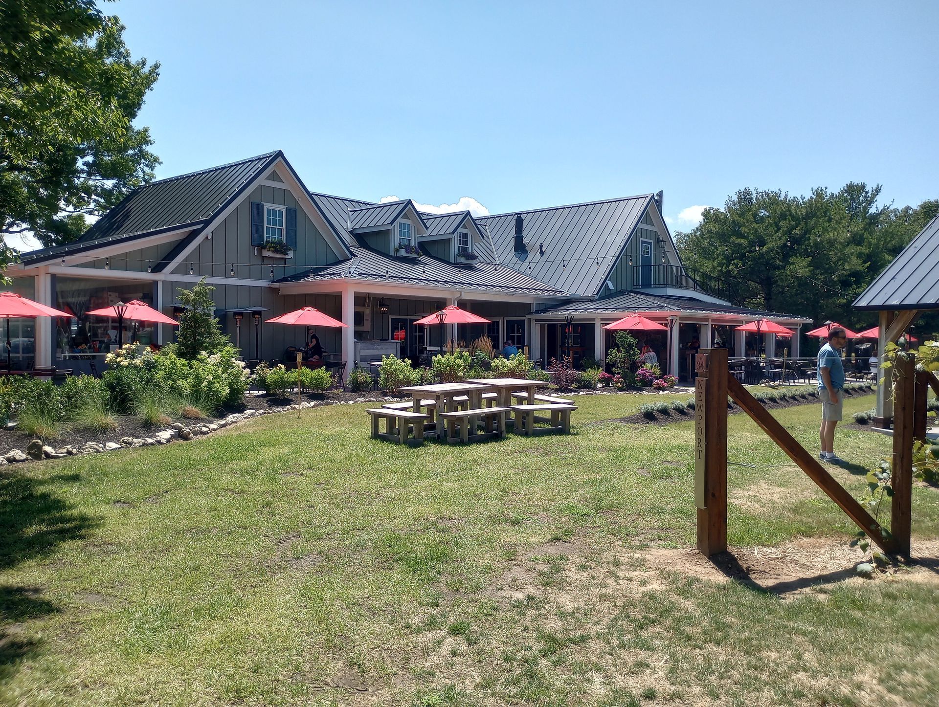 Outdoor patio of a restaurant with red umbrellas, a wooden table, and a grassy lawn on a sunny day.