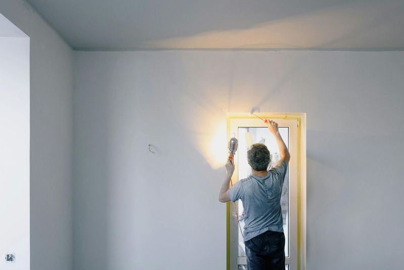 Person sanding wall near doorway, light from outside shining in.