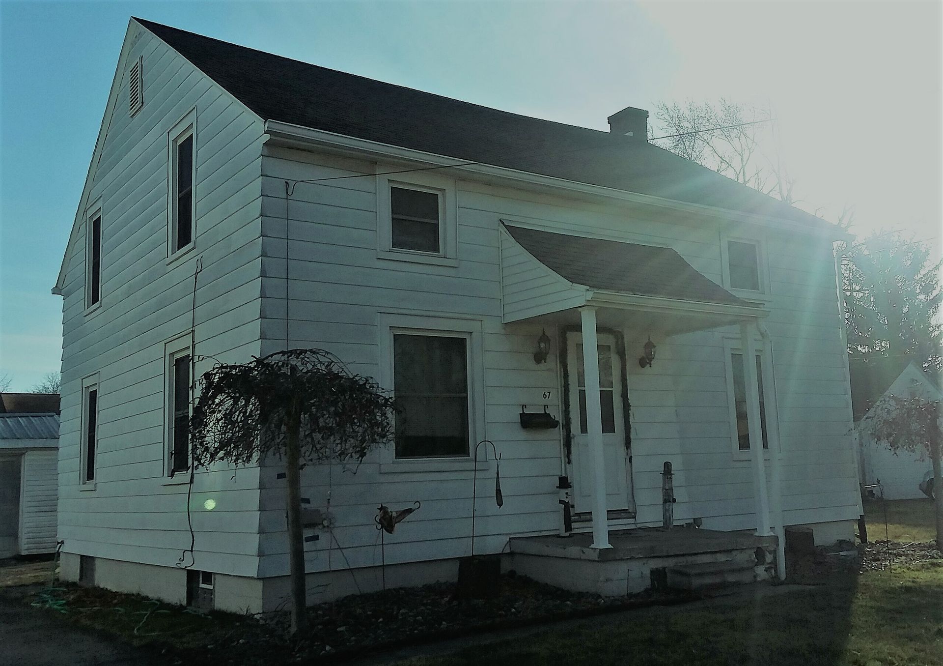 A two-story white house with a gabled roof and a small front porch, bathed in soft afternoon sunlight.
