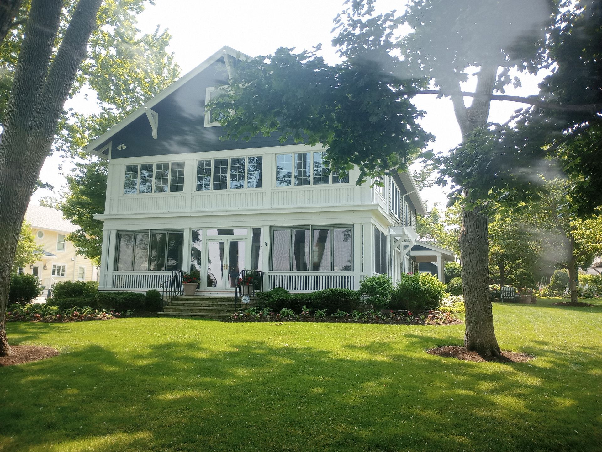 A large, two-story house with white siding and a dark blue gable, set behind a lawn with mature trees.