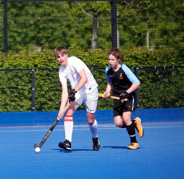 Two boys are playing field hockey on a blue field