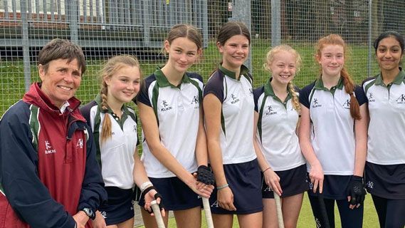 A group of young girls are standing next to each other on a field holding hockey sticks.