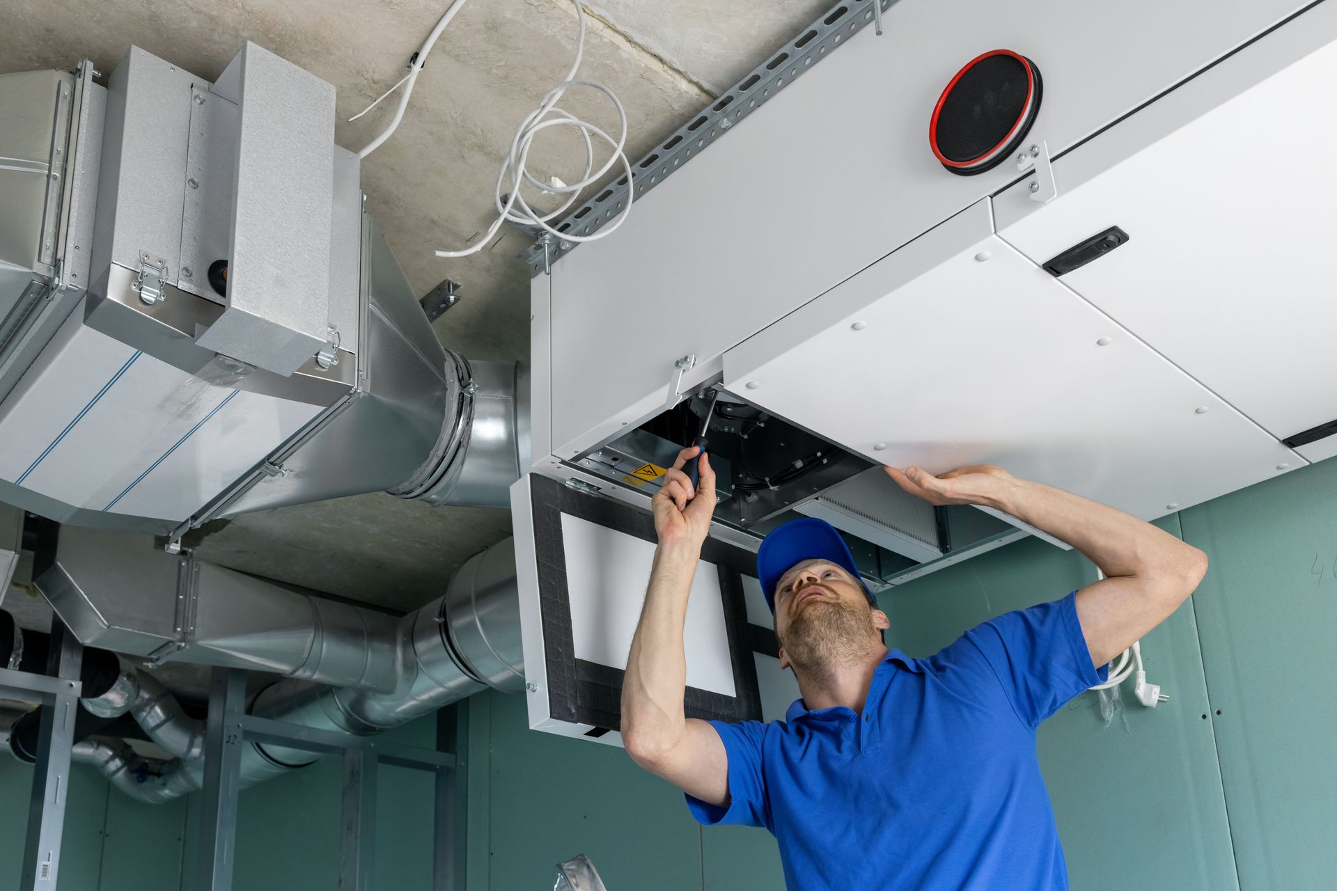 Worker in a blue shirt installing ductwork in a ceiling crawlspace