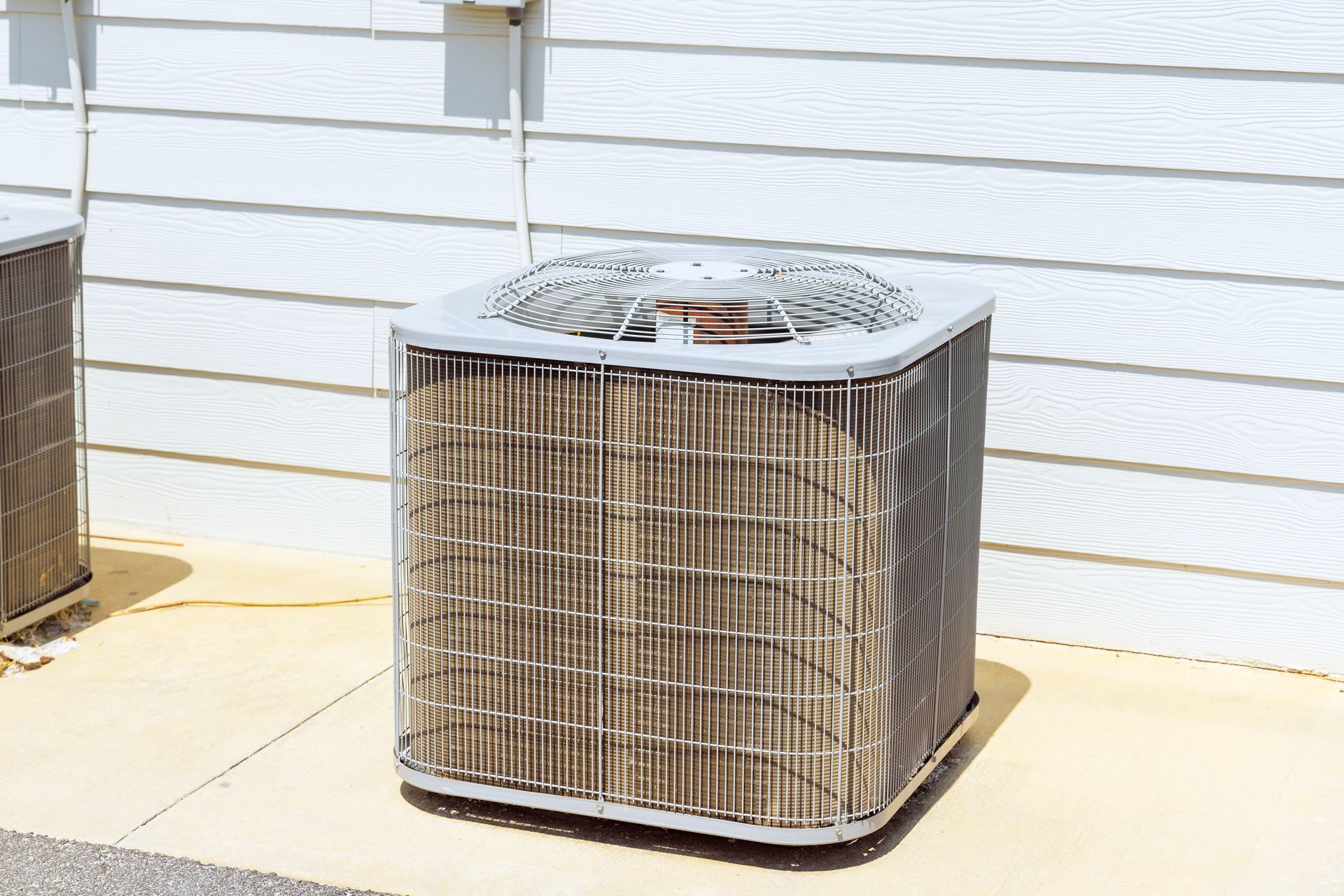 A beige outdoor air conditioning unit sits on a concrete pad against white horizontal siding.