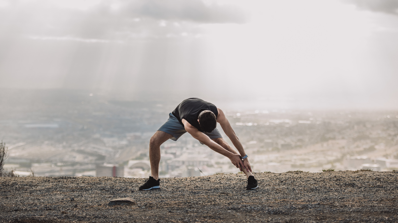 Man stretching legs outdoors with a city view.