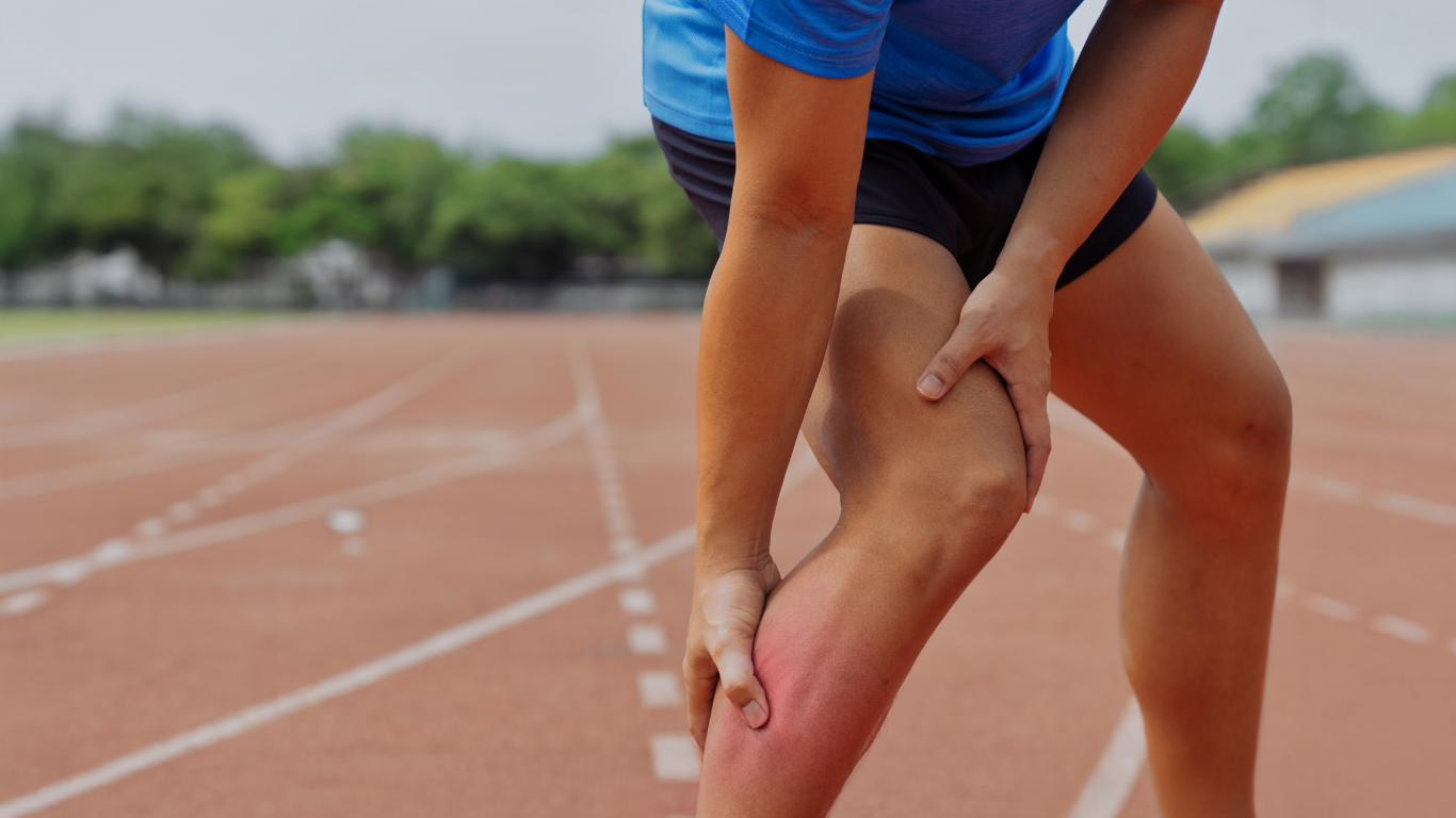 Athlete clutching leg, appearing in pain, on a running track. Red, irritated skin visible.