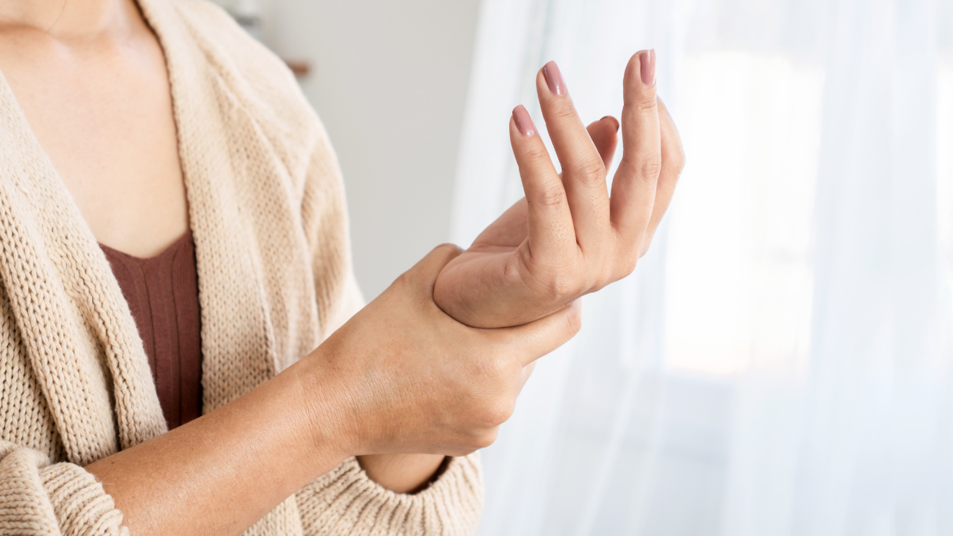 Woman holding wrist, possibly in pain, indoors, wearing a light cardigan.