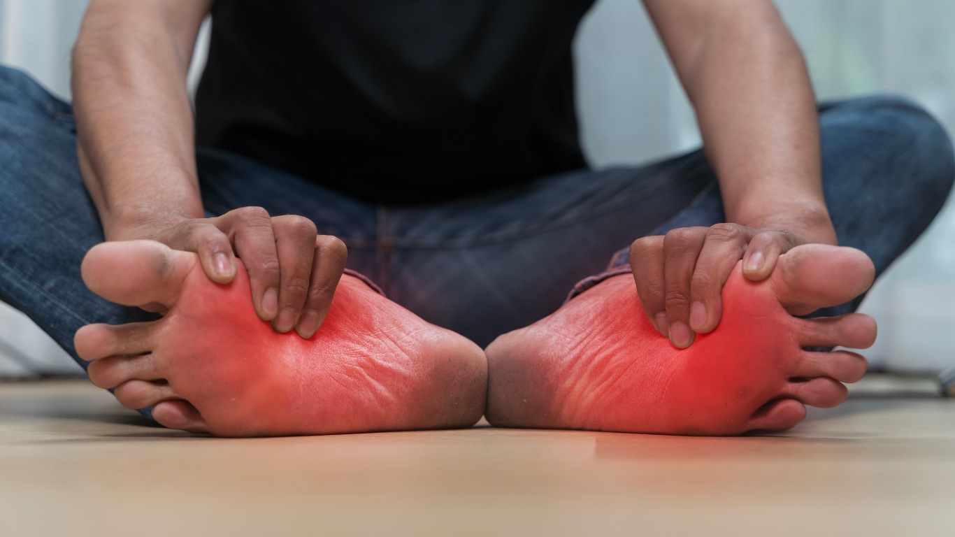 Person sitting, hands on feet, indicating foot pain; red discoloration.