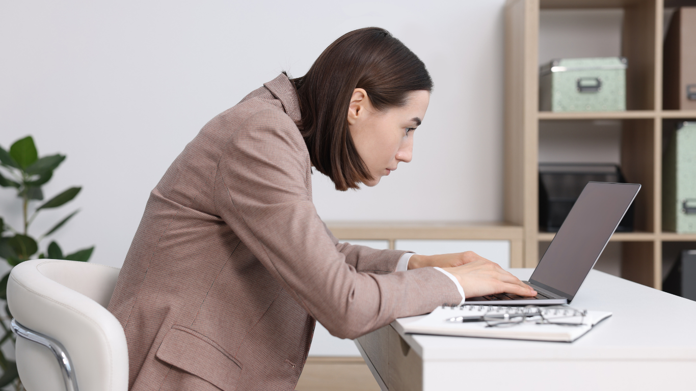 Woman hunched over a laptop, working at a desk in an office.