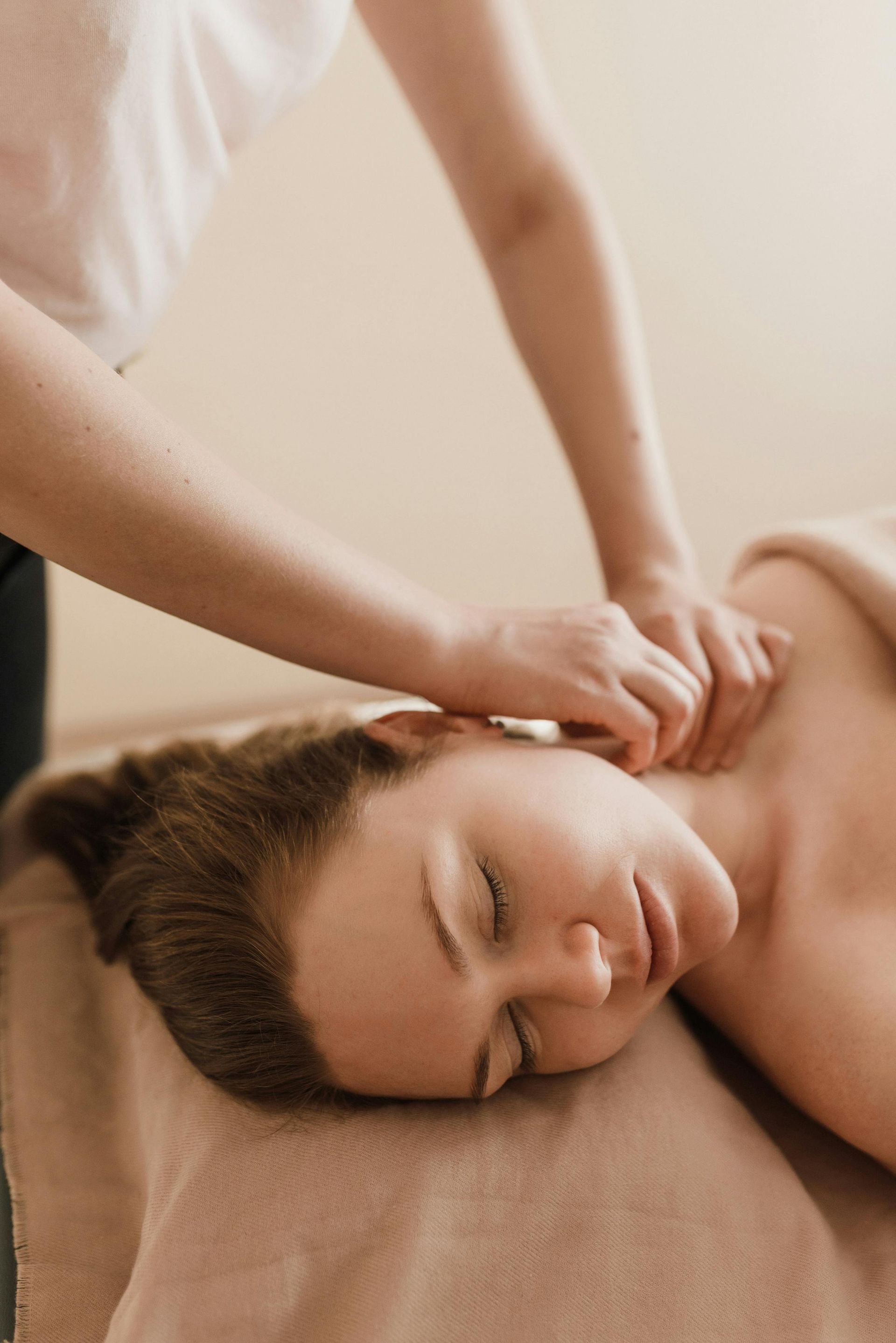 Person receiving a neck massage at a spa. Hands kneading shoulders; person relaxing with eyes closed.