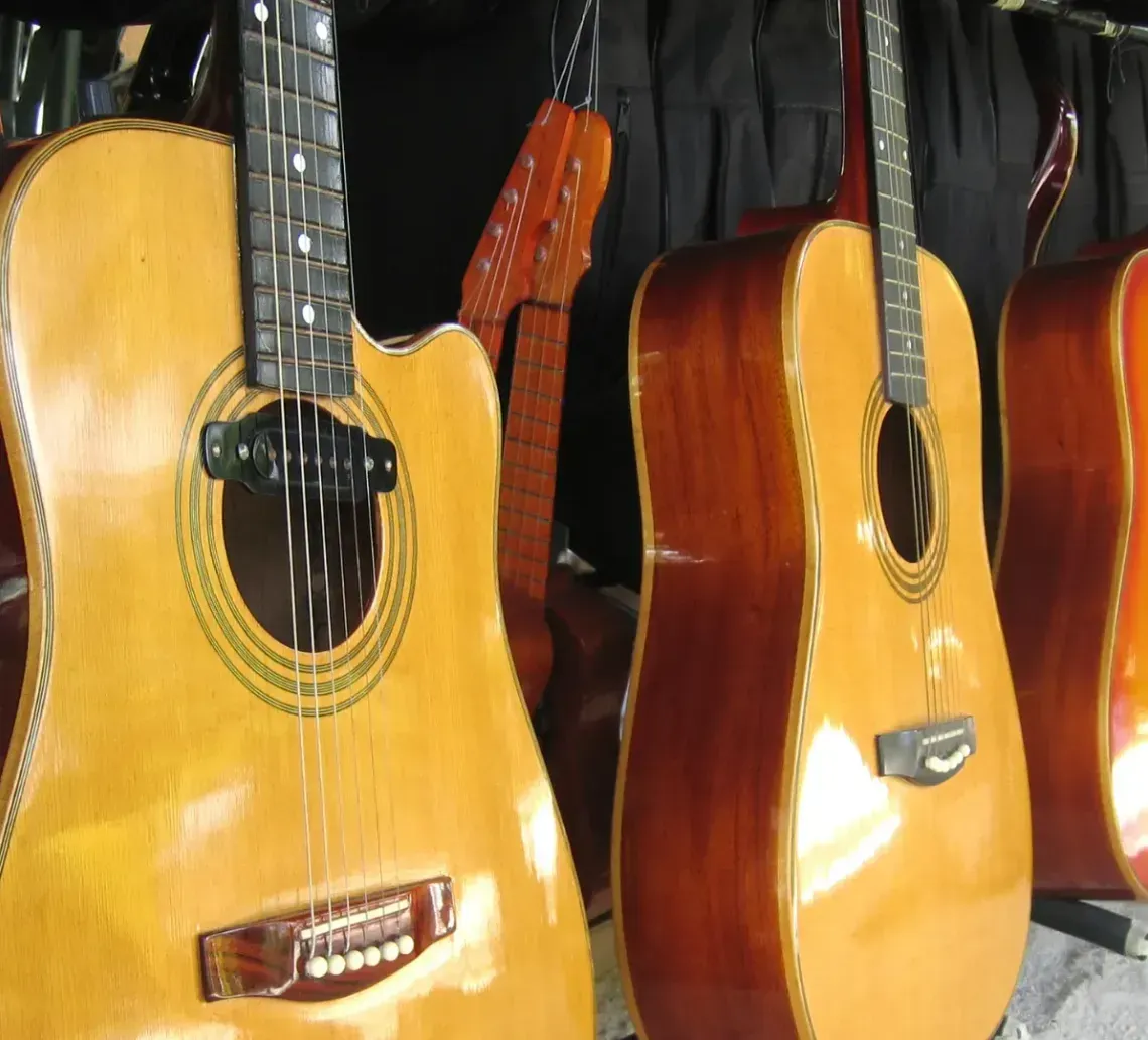 A row of wooden acoustic guitars hanging in a shop, ranging from light to dark wood finishes.