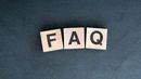 The letters F, A, and Q on wooden blocks arranged in a row against a dark, textured background.
