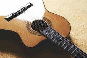 A close-up of a light-brown acoustic guitar resting on a textured, neutral-colored surface.