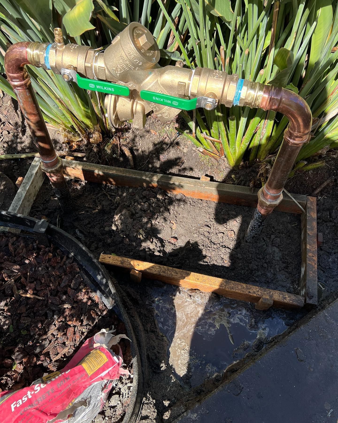 Copper water pipe assembly with green handles and a metal frame, set in soil.