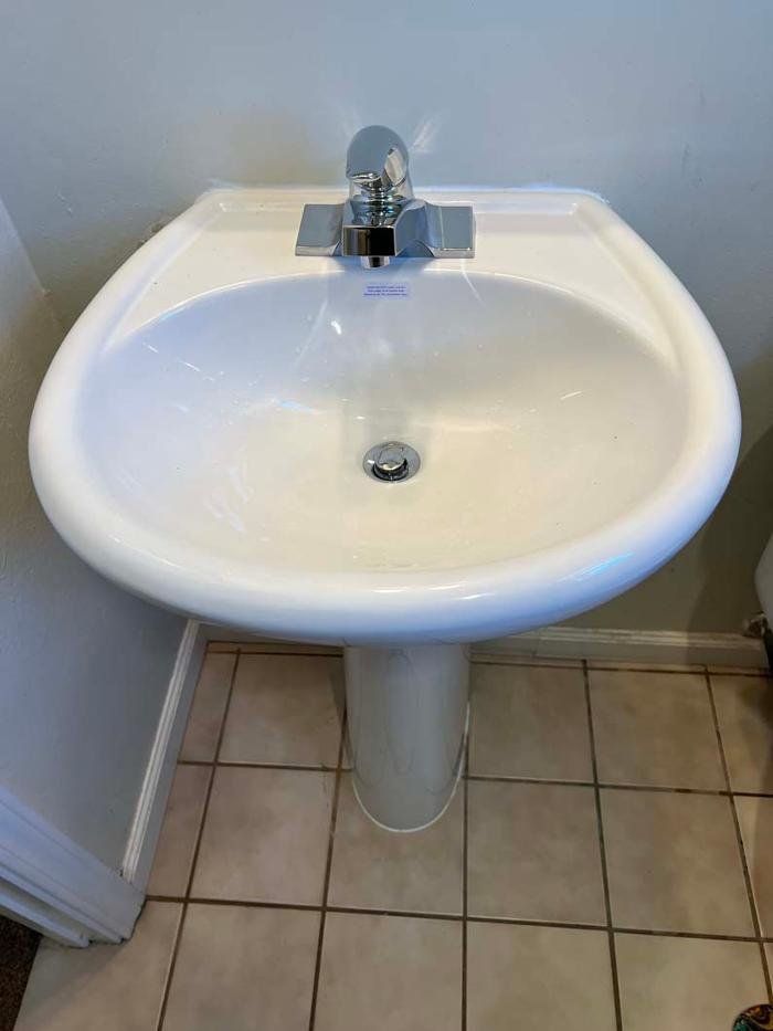 White pedestal sink with chrome faucet and drain in a bathroom.