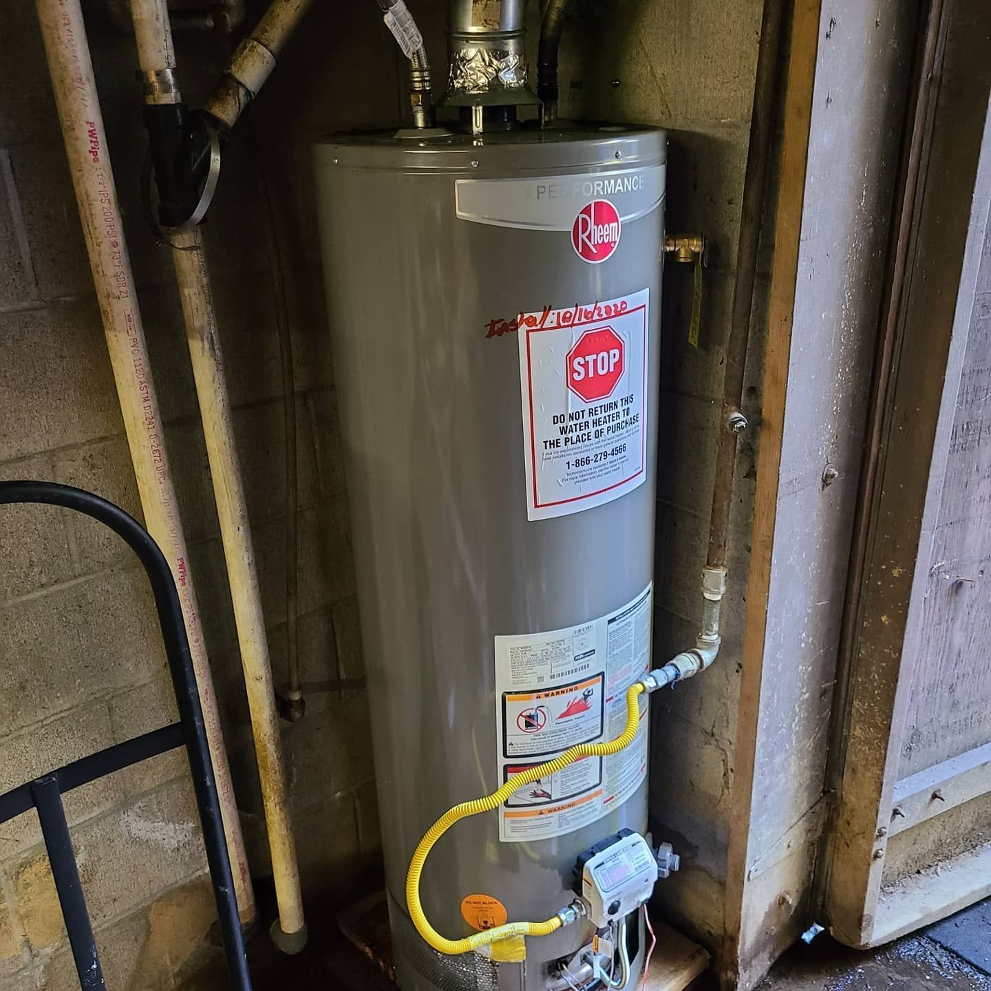 A Rheem water heater in a basement setting, with a yellow gas line and pipes visible.