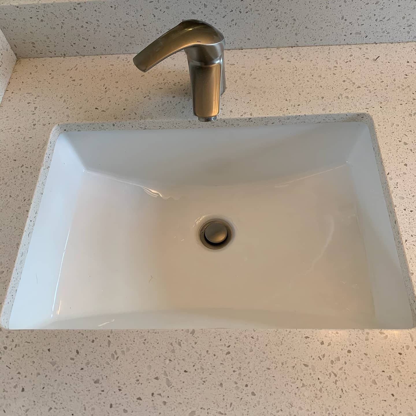 White rectangular bathroom sink with silver faucet on a speckled countertop.