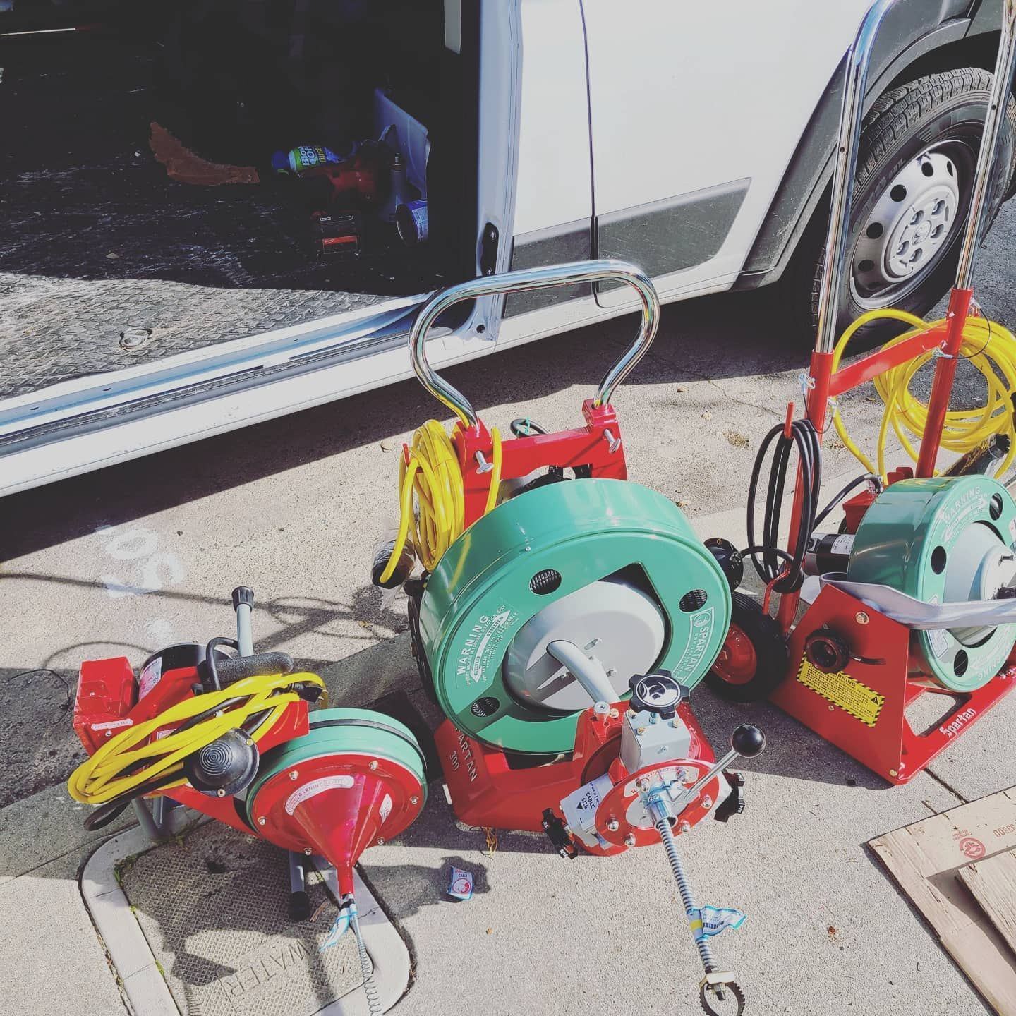 Three red and green drain cleaning machines sit outside a van.