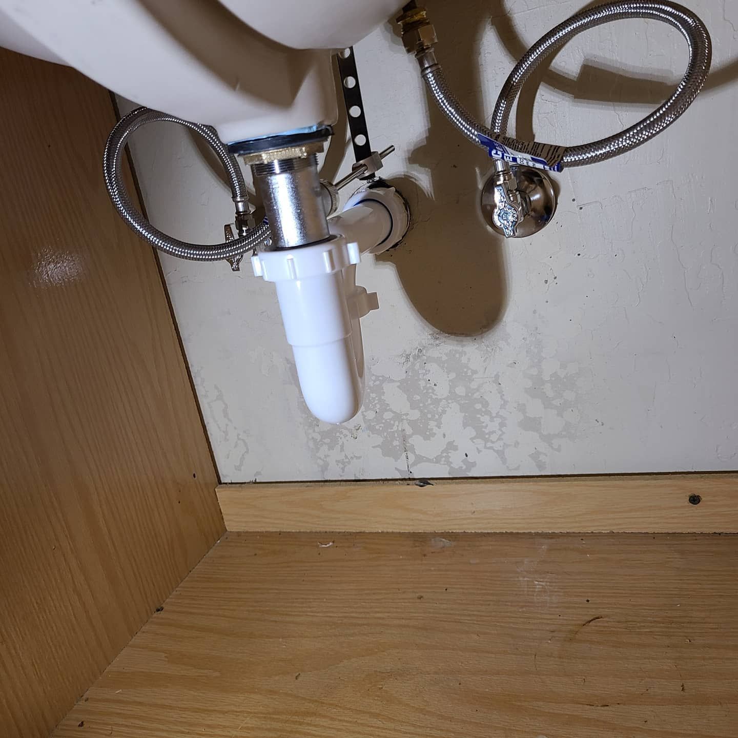 Under-sink plumbing: chrome water lines, white drainpipe, and a partially visible wooden cabinet.