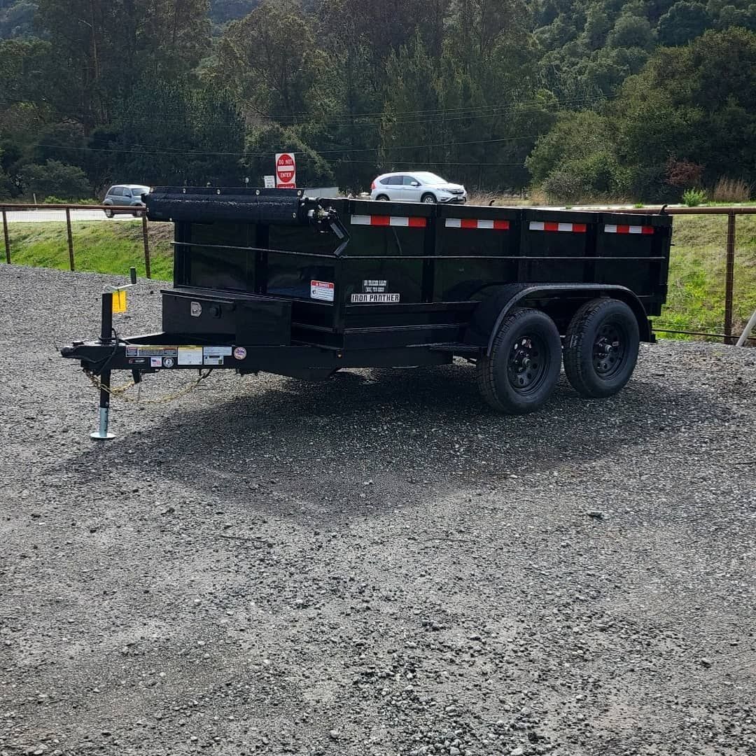 Black dump trailer on gravel, with two wheels and safety stripes, outdoors.