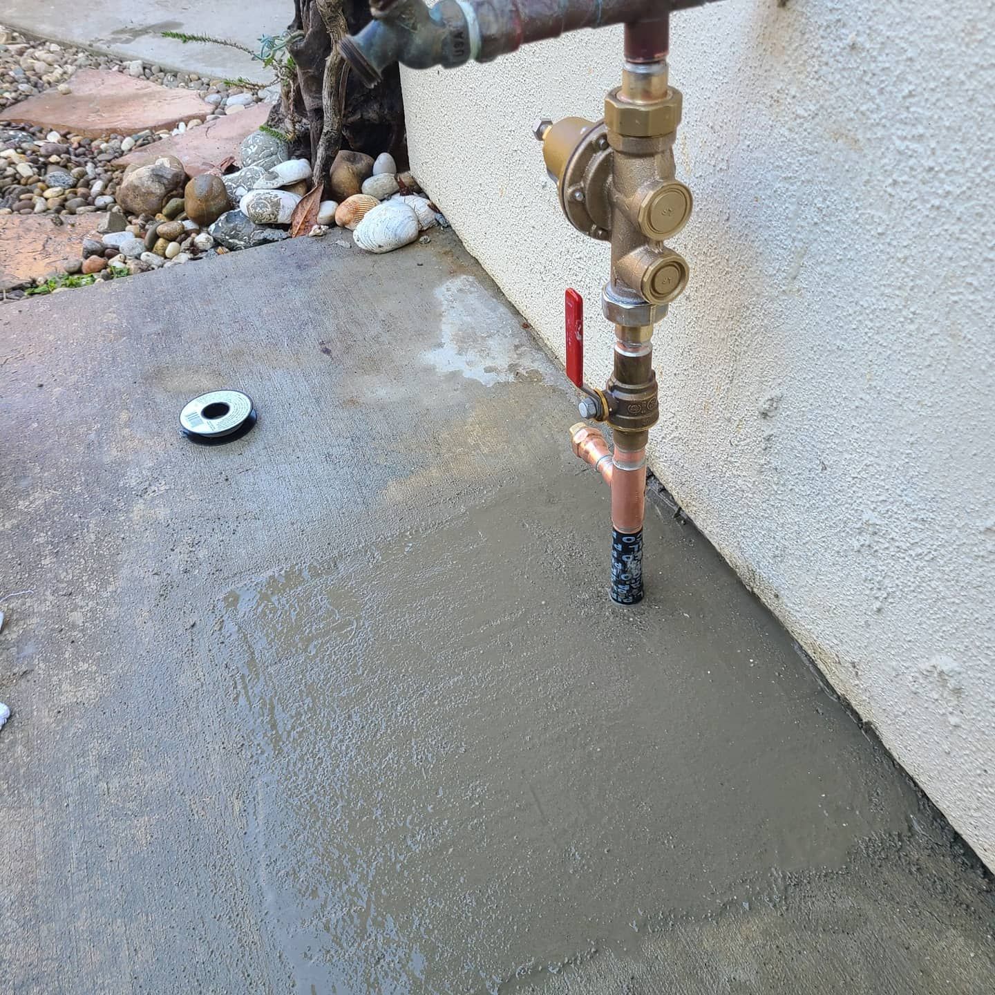 Concrete slab with plumbing pipes and valve against a white stucco wall.