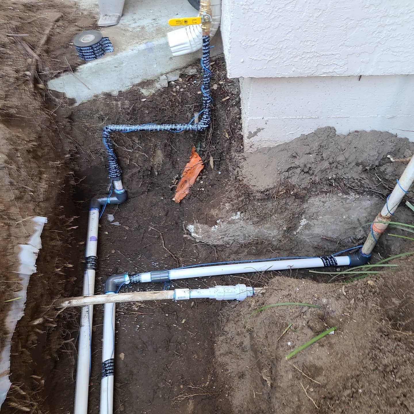 Underground plumbing with various pipes and fittings installed near a building's foundation.
